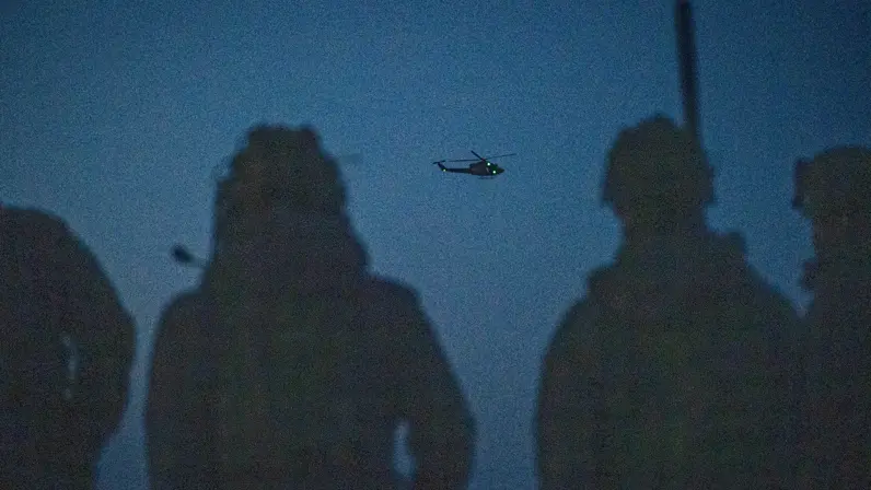 Twee FST-leden met een helikopter in de lucht op de achtergrond. 