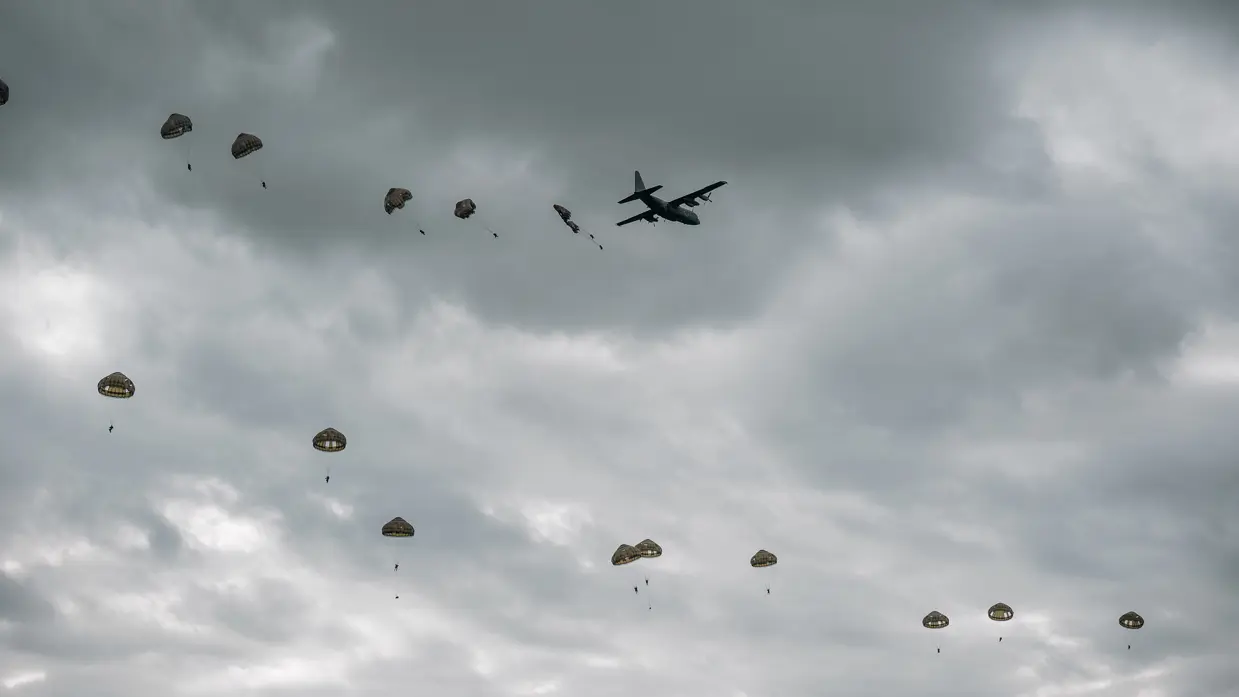 Tientallen parachutisten hangen in de lucht nadat ze uit een vliegtuig zijn gesprongen.