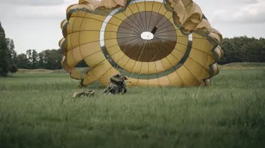 Een parachutist die net is geland in het gras probeert zijn parachute onder controle te krijgen.