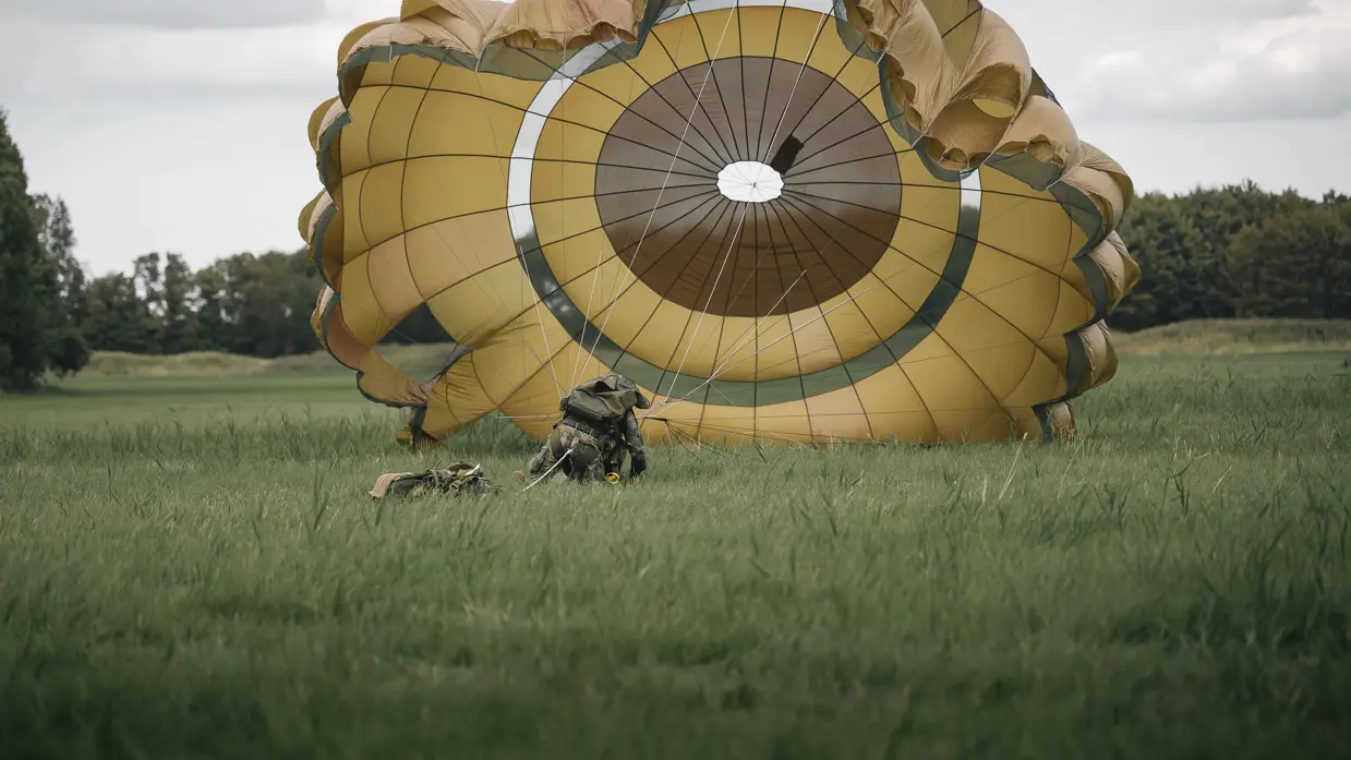 Een parachutist die net is geland in het gras probeert zijn parachute onder controle te krijgen.