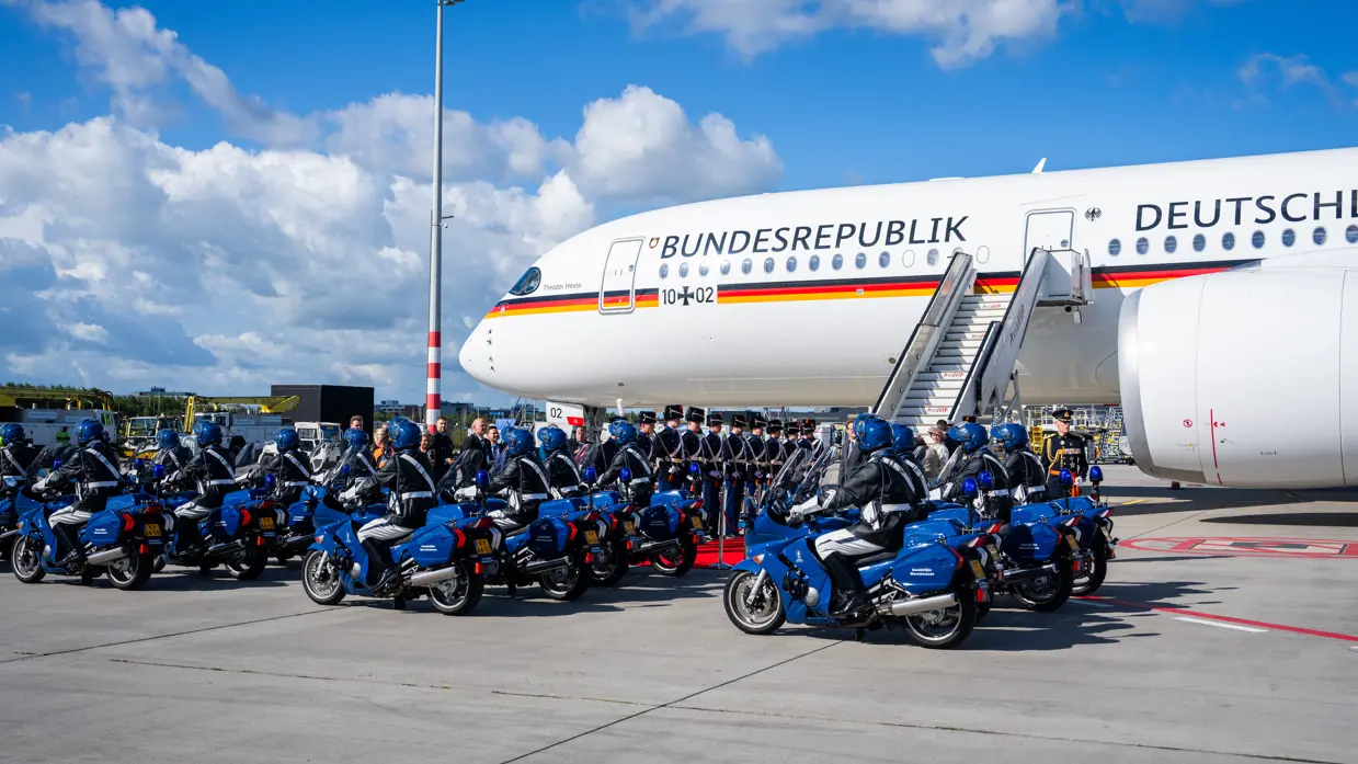 Motorrijders en Marechaussees in ceremonieel tenue voor het Duitse regeringsvliegtuig.