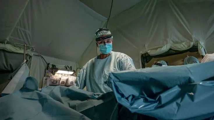 Een arts met mondmasker en lichtgroene kleding kijkt naar een patiënt.