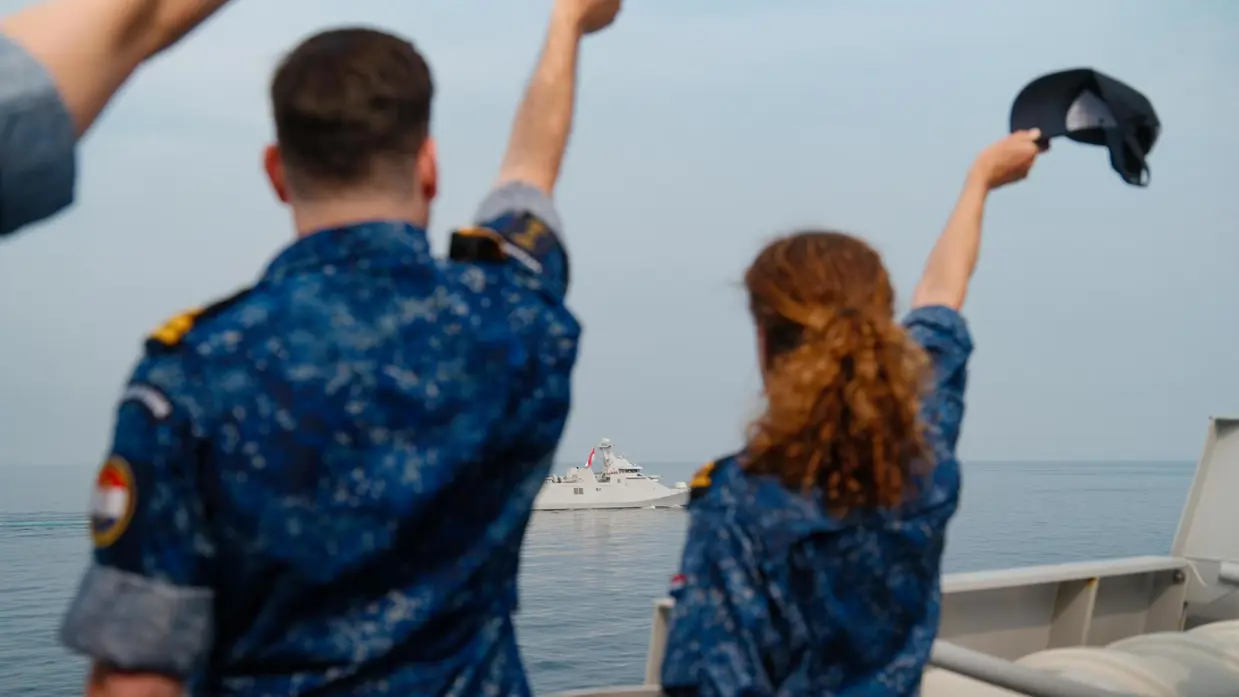 Twee Twee militairen zwaaien een schip op de horizon uit vanaf de haven.