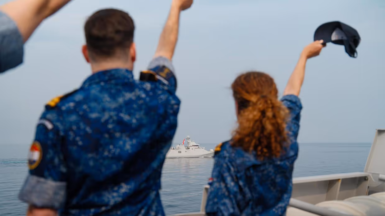 Twee Twee militairen zwaaien een schip op de horizon uit vanaf de haven.