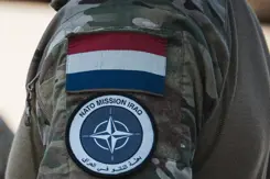 Schouder militair met NAVO-embleem en Nederlandse vlag erboven.