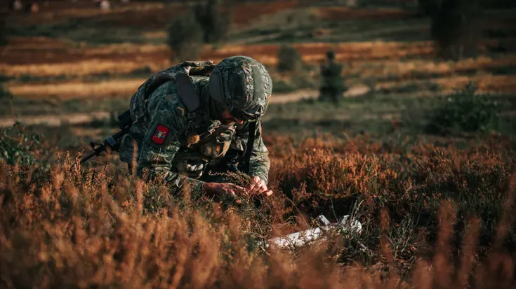 Een EOD'er zittend tussen de heide met voor hem een explosief.