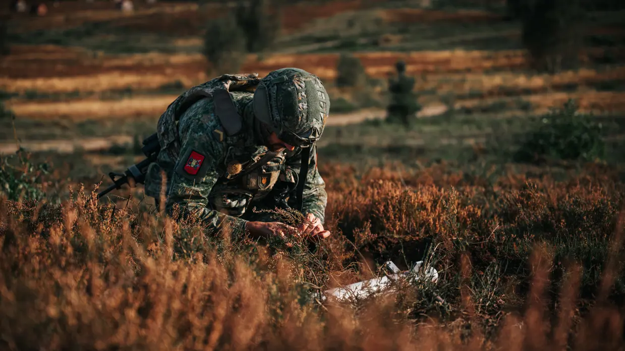Een EOD'er zittend tussen de heide met voor hem een explosief.