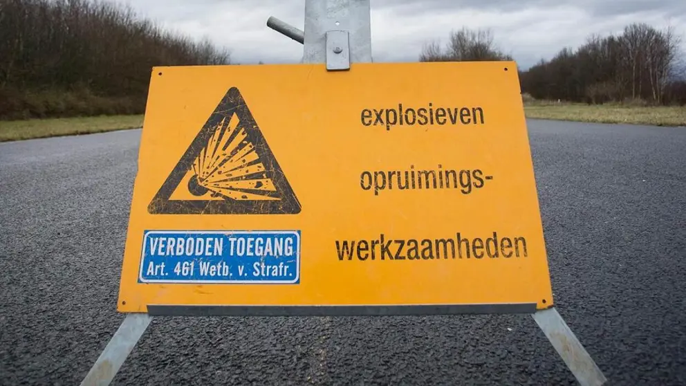 Geel bord op de weg met de tekst: explosieven opruimingswerkzaamheden en  verboden toegang.