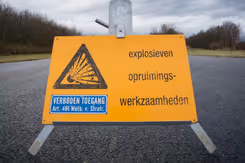 Geel bord op de weg met de tekst: explosieven opruimingswerkzaamheden en  verboden toegang.