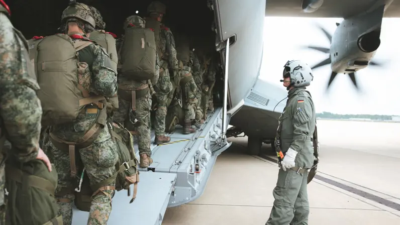 Militairen met parachute-uitrusting lopen via de laadklep een Duits A400M-transportvliegtuig binnen, terwijl een bemanningslid toezicht houdt naast het toestel.&nbsp;