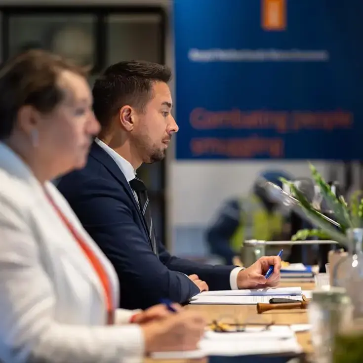 Twee personen achter een tafel met microfoons.