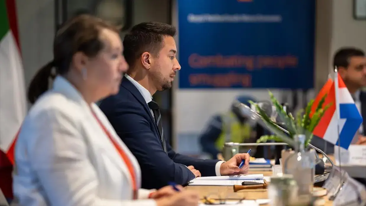 Twee personen achter een tafel met microfoons.