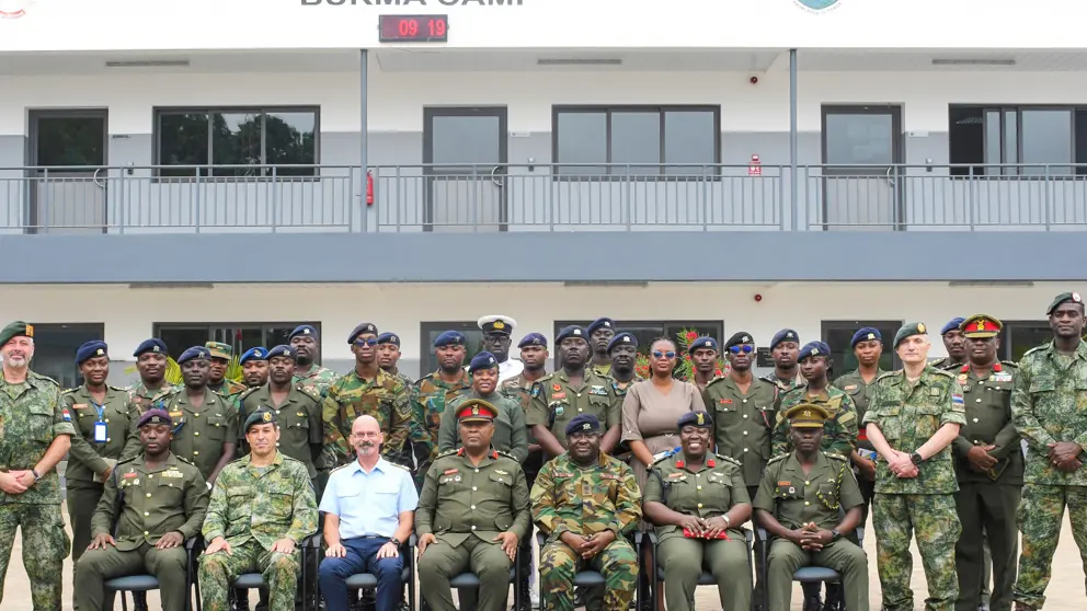 Groepsfoto van Nederlandse trainers en lokale militairen voor een trainingslocatie. 