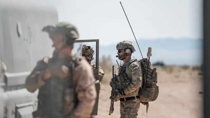 Drie militairen in de woestijn staan bij een voertuig.