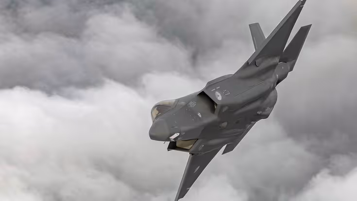 F-35 schuin in een bocht met op achtergrond dik grijs wolkendek.