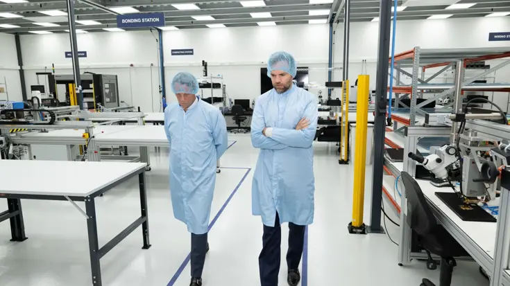 Twee mannen lopen in beschermende kleding door een fabriekshal.
