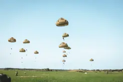 Parachutisten in de lucht boven grasveld.