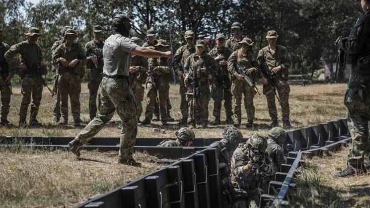 Instructeur geeft aanwijzingen aan militairen tijdens training in loopgraaf.