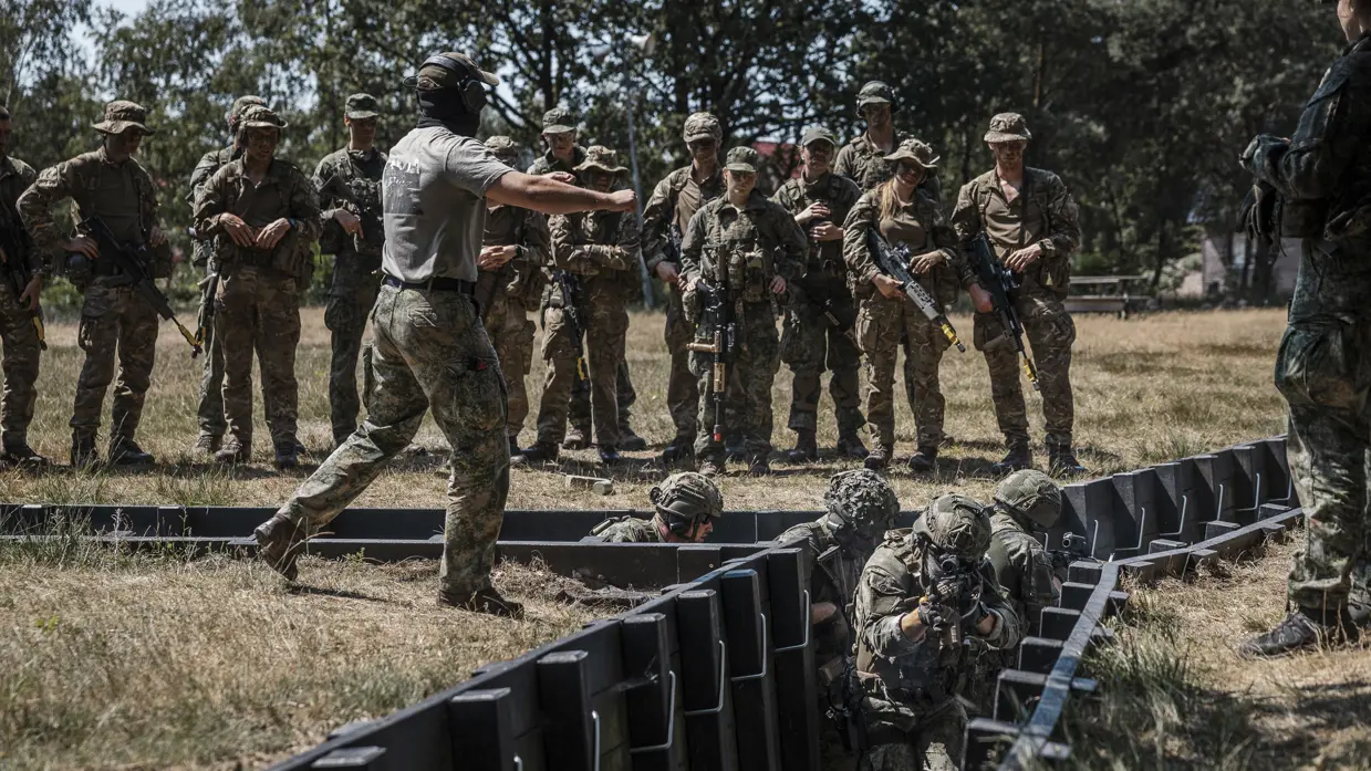Instructeur geeft aanwijzingen aan militairen tijdens training in loopgraaf.
