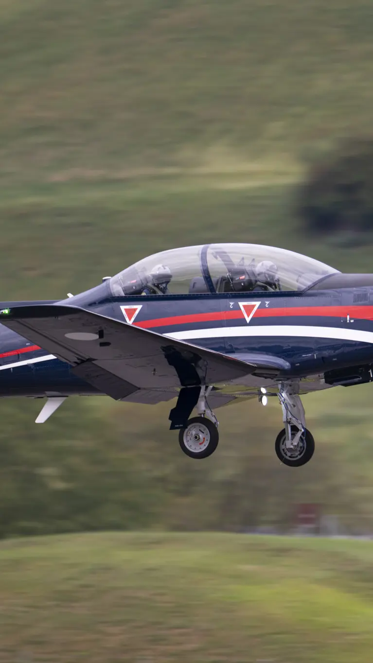 De PC-7 MKX vliegt boven voor een groene achtergrond.