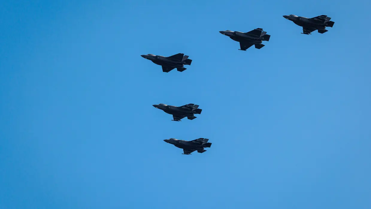 Vijf F-35 gevechtsvliegtuigen tegen een blauwe hemel.   