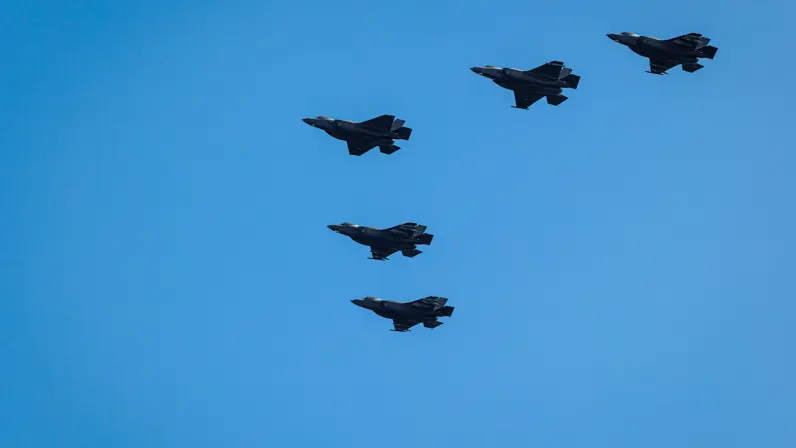 Vijf F-35 gevechtsvliegtuigen tegen een blauwe hemel.   