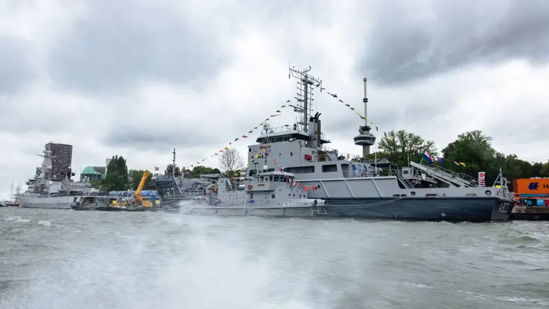 Zr.Ms. Luymes ligt aan de kade, ervoor varen kleinere schepen.