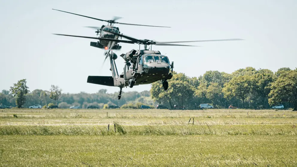2 helikopters vliegen laag boven grasland.