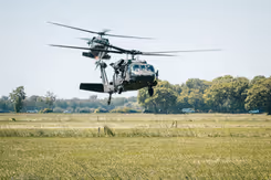 2 helikopters vliegen laag boven grasland.