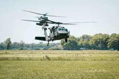 2 helikopters vliegen laag boven grasland.