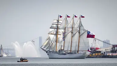 zijaanzicht van een groot wit zeilschip van de Amerikaanse Kustwacht met op de achtergrond de bebouwing van Manhattan.