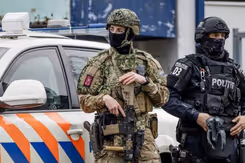 En gewapende, gemaskerde militair staat voor een politieauto en naast een politieman met gezichtsbedekking.