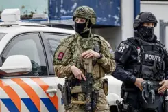 En gewapende, gemaskerde militair staat voor een politieauto en naast een politieman met gezichtsbedekking.