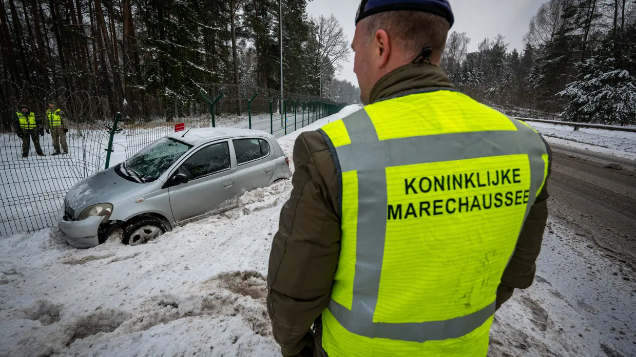 een marechaussee die kijkt naar een van de weg geraakte auto.  