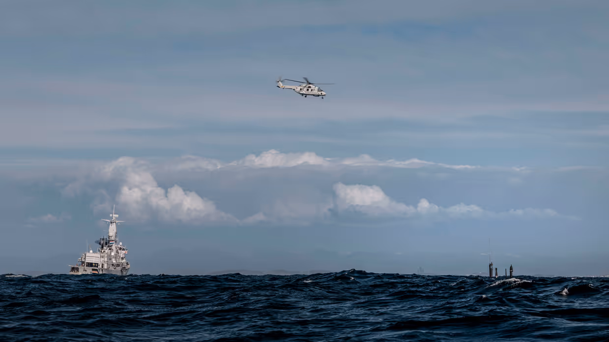 Marineschip en onderzeeboot op zee, met maritieme gevechtshelikopter erboven.