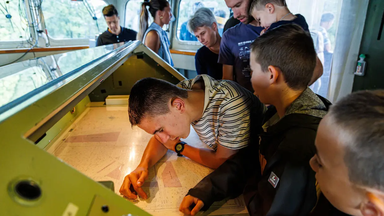 Jonge bezoekers kijken op de brug van een schip naar een zeekaart.&nbsp;