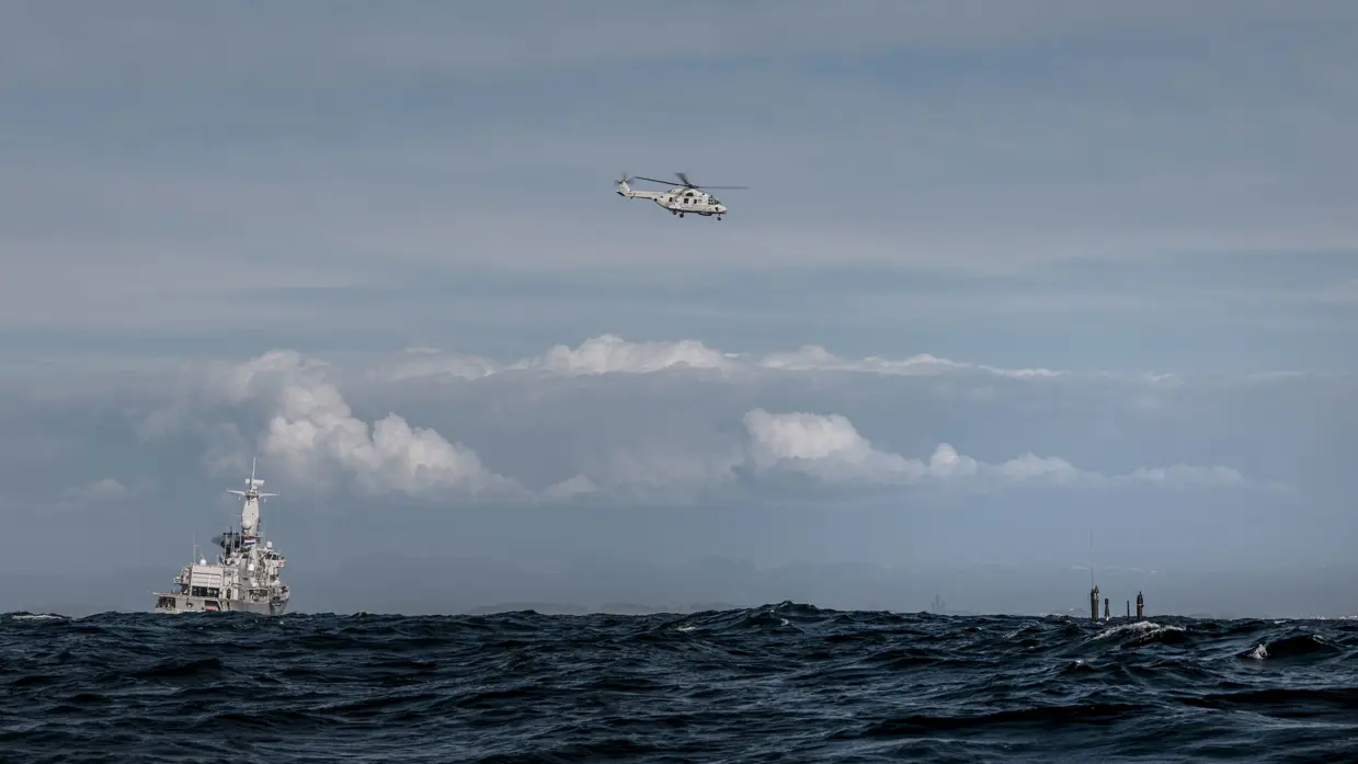 Marineschip en onderzeeboot op zee, met maritieme gevechtshelikopter erboven.