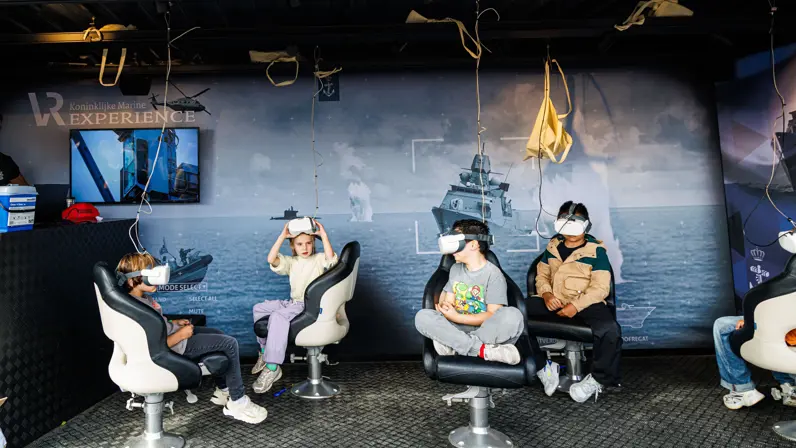 Vier jongeren die in een open studio met een VR-bril op het gezicht op stoelen zitten. 