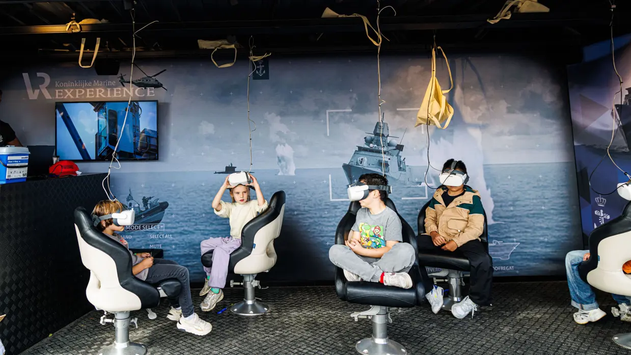Vier jongeren die in een open studio met een VR-bril op het gezicht op stoelen zitten. 