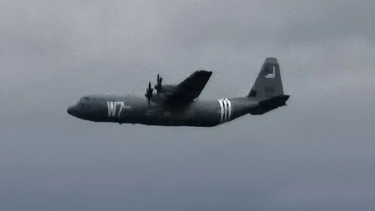 een C130 Hercules voorzien van geallieerde herkenningsstrepen tegen een donkere achtergrond.