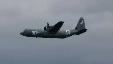 een C130 Hercules voorzien van geallieerde herkenningsstrepen tegen een donkere achtergrond.