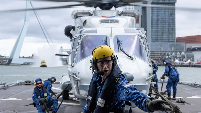 De heli met draaiende rotorbladen en aan weerszijden marinepersoneel. 