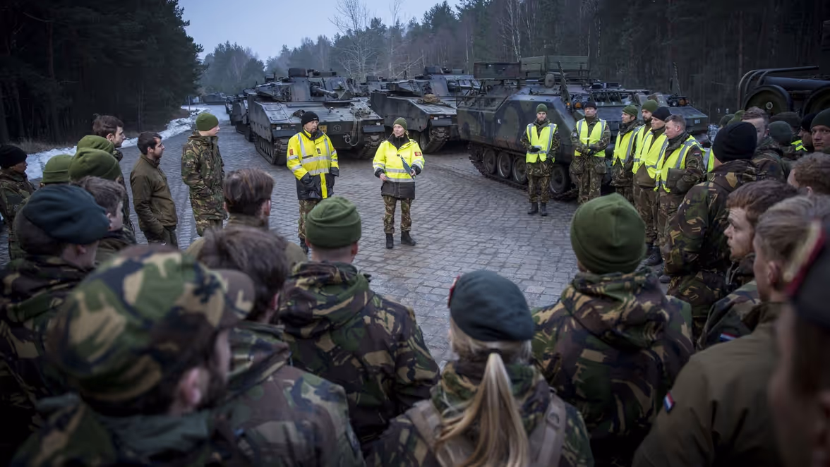 Militairen luisteren in kring naar collega's met gele hesjes.