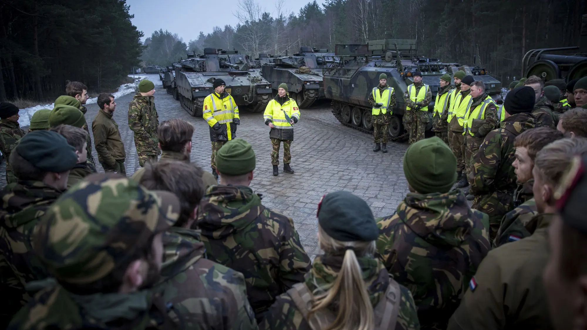 Militairen luisteren in kring naar collega's met gele hesjes.