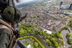 Gehelmde man kijkt vanuit een helikopter naar bebouwd gebied aan een rivier.