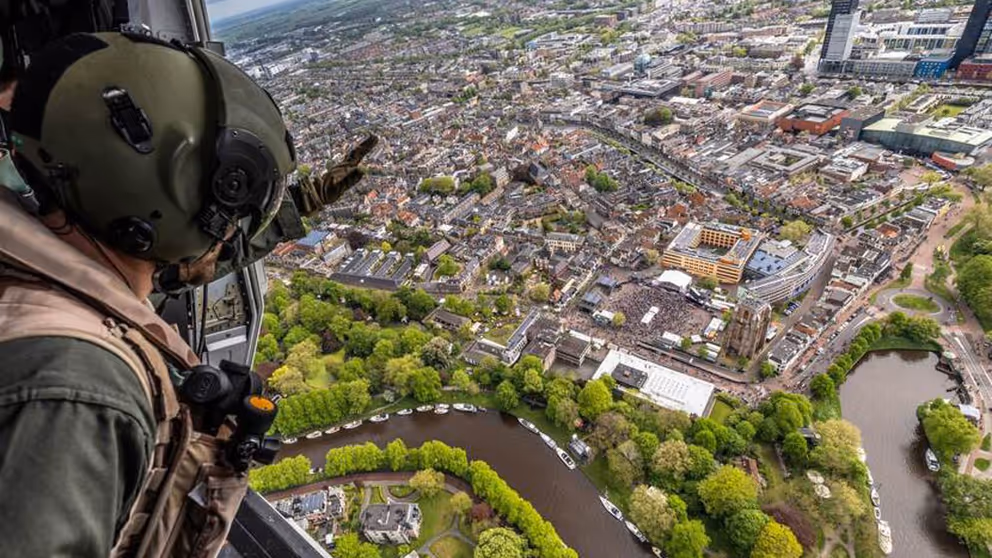 Gehelmde man kijkt vanuit een helikopter naar bebouwd gebied aan een rivier.