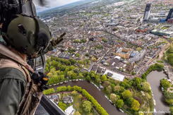 Gehelmde man kijkt vanuit een helikopter naar bebouwd gebied aan een rivier.