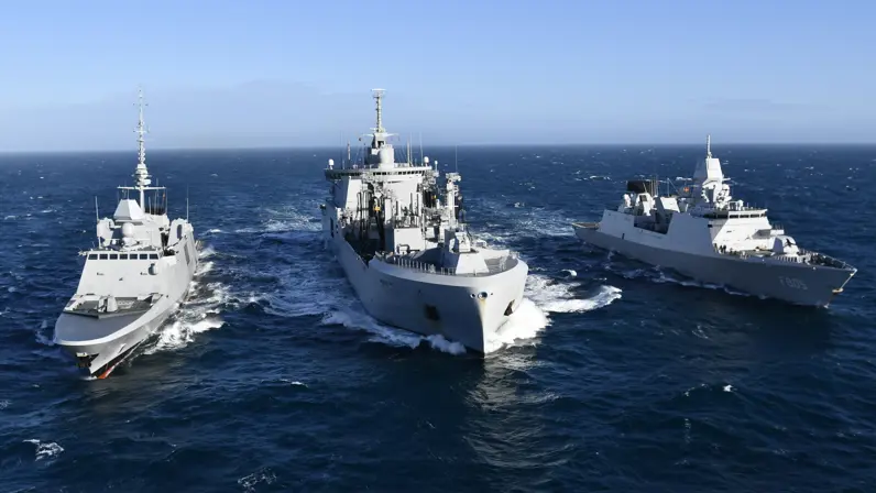 Twee fregatten varen aan weerszijde van een bevoorrader. 