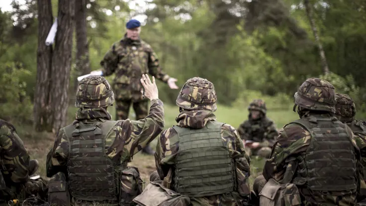 Leerlingen in camouflagepak luisteren naar docent.