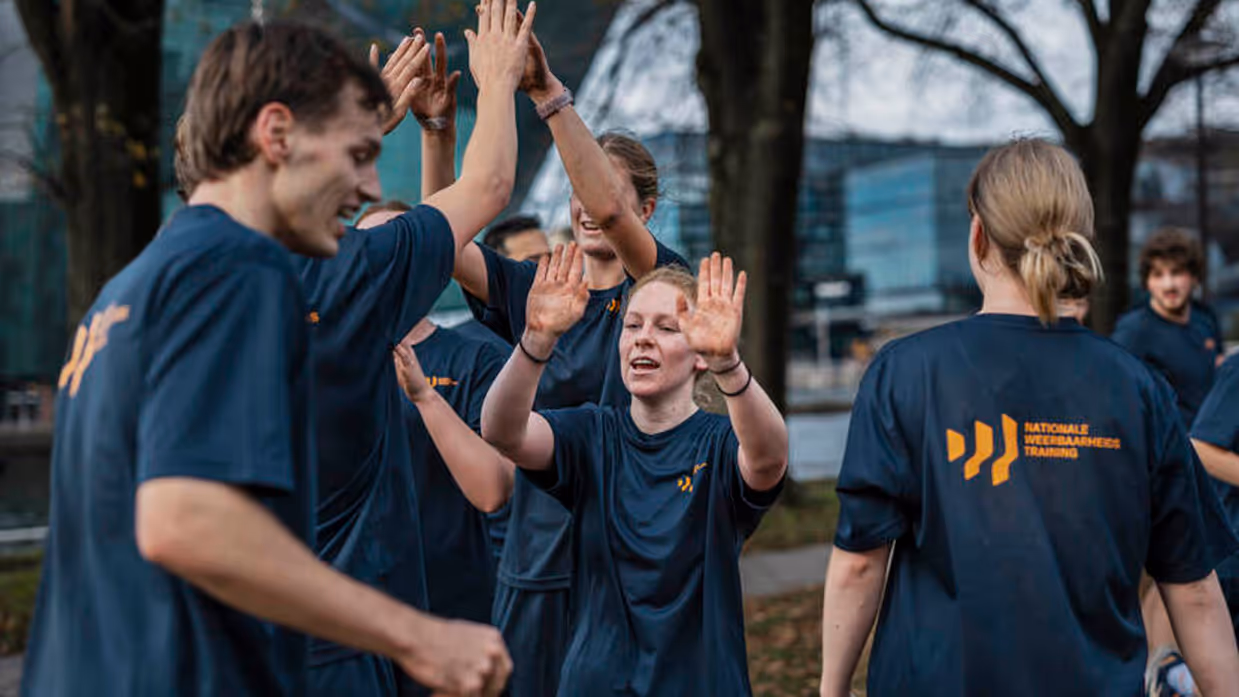 Jongeren geven elkaar high five. Op hun T-shirt staat de tekst Nationale Weerbaarheids Training. 